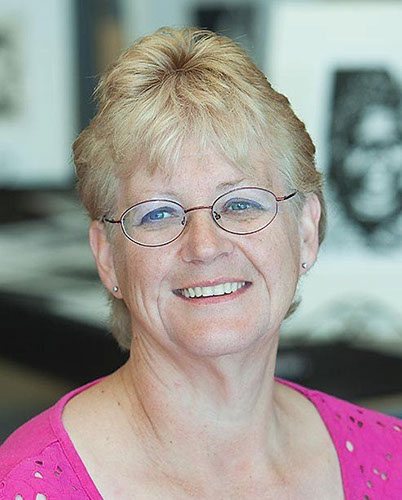 Linda Abblitt, wearing pink knitted top, looking towards the camera, blurred background.